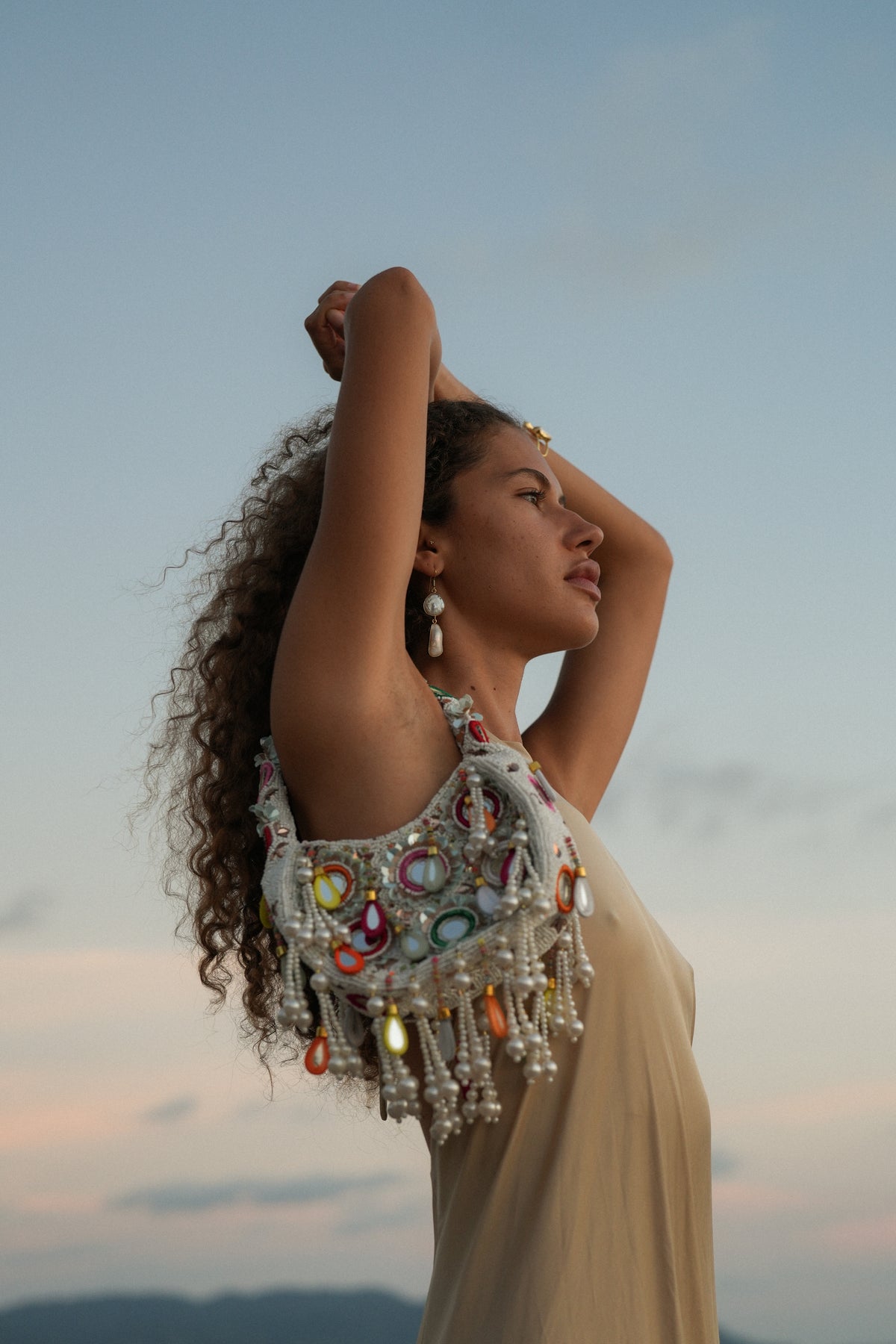 Woman wearing ivory Formentera beaded statement bag with pearl fringe and mirror accents, Mediterranean summer style